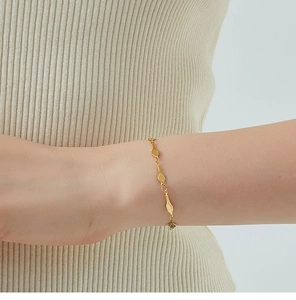 Detail shot of a gold tennis racket bracelet worn over a beige knit sleeve for a chic look