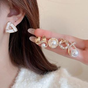 Detail of elegant gold earrings set with pearls and rhinestones on model's ear and hand