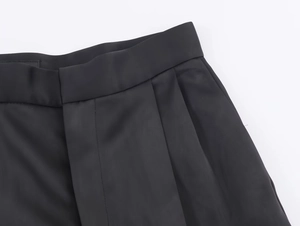 Dettaglio dei pantaloni in raso nero con pieghe precise e sartoria a vita alta