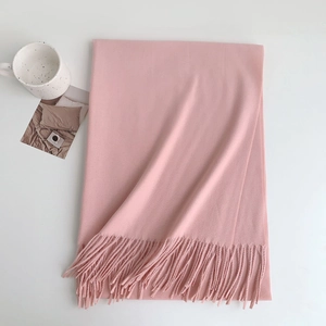 Close-up of soft pink cashmere-style scarf featuring fringe edges and decorative props