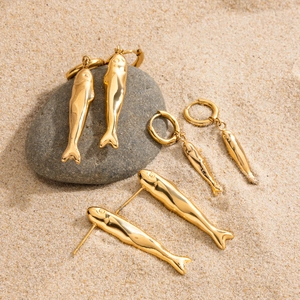 Three pairs of golden stainless steel fish-shaped earrings displayed on a natural rock surface
