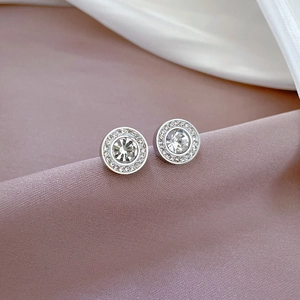 Macro shot of silver circular stud earrings with clear crystals on silk fabric