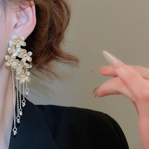 Close-up of golden flower and butterfly tassel earrings worn with elegant chain fringe