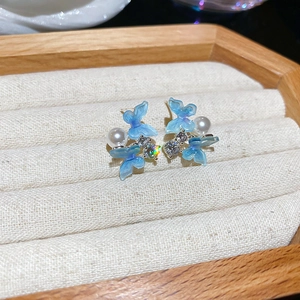 Détail de boucles d'oreilles papillon bleu avec perles et cristaux sur plateau velours