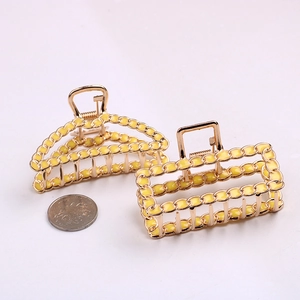 Detailed view of large gold hollow geometric hair claws with yellow finish and scale coin