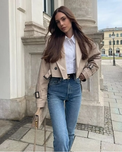 Trench corto kaki da donna abbinato a jeans blu a vita alta e borsa a mano color beige