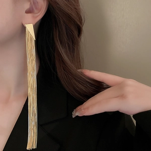 Close-up of long gold fringe tassel earrings with geometric triangle top worn by a model