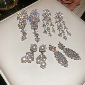 Detail of silver needle earrings with zircon flower tassels and pearls on white leather