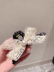 Détail d'une pince à cheveux en dentelle florale avec nœud beige et perle à la main