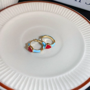 Détail de créoles en émail bleu clair avec motif cœur rouge sur une assiette en céramique