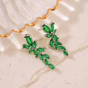 Elegant floral zircon earrings with emerald green stones on a white textured background