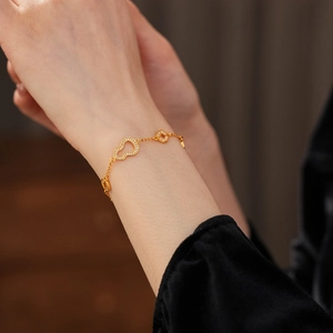 Detailed close-up of a 24k gold plated bracelet with gourd and coin charms on a wrist
