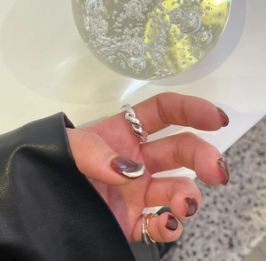 Detailed view of silver twisted rope rings worn on fingers with minimalist glass decor