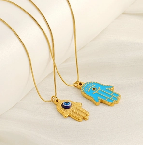 Detailed close-up of golden Hamsa Hand pendants with blue Evil Eye on white silk