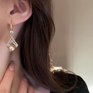 Close-up of golden triangle earrings featuring sparkling rhinestones and a faux pearl drop