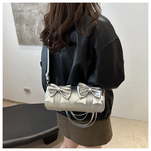 Model wearing silver cylinder bag with large bows and chain handle in a bright interior