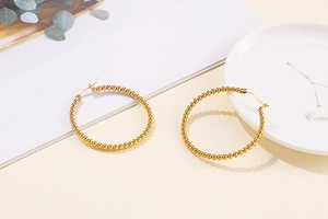 Detail of gold beaded hoop earrings made of stainless steel on a white porcelain dish