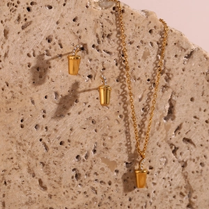 Detailed view of gold necklace and earrings set with crystal cola cup charms on stone