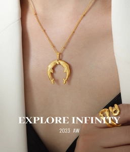 Detail showing a golden whale pendant necklace and spiral ring worn with a blazer