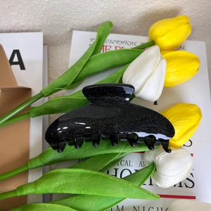 Detail of a large black semi-circular hair claw clip with fine silver glitter accents