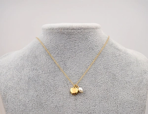 Détail du collier coeur doré avec petite perle blanche sur un buste en velours gris