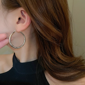 Close-up of model wearing large gold hoop earrings with textured hammered metal finish