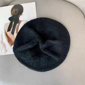 Close-up of soft black mohair knit beret texture on minimalist grey leather background