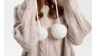 Close-up of beige cable knit texture and soft white faux fur pom poms on the winter hat