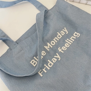 Detail of light blue denim tote bag with Blue Monday Friday feeling white embroidery