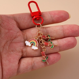 Rainbow cloud and red rose enamel keychain with metal hook held against pink background