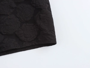 Detail eines schwarzen Jacquard-Kleides mit Rosenmuster-Prägung und hochwertigem Saumabschluss