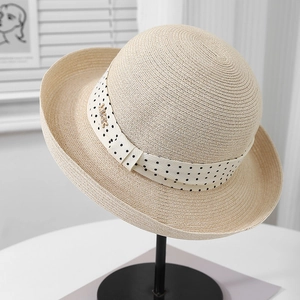 Detail of French straw hat with polka dot ribbon and gold metal charm on a hat stand
