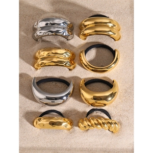 Detailed assortment of 18k gold and silver arched metal hair ties on sand background