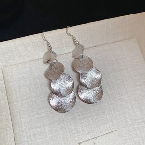 Macro detail of silver irregular matte disc fringe earrings on a beige textured surface