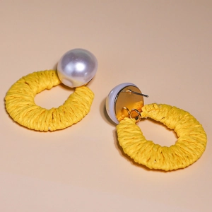 Detailed view of yellow raffia woven hoop earrings featuring large white faux pearls
