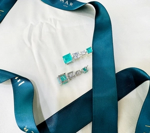 Close-up of emerald and cubic zirconia earrings on silk ribbon and beige background