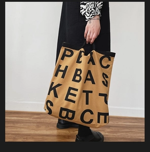 Detailed close-up of a large yellow-brown canvas tote bag with black letter print details