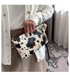 Close-up of cow print envelope clutch with gold zipper and leather tassel detail