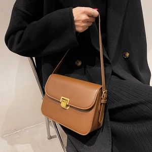 Elegante borsa a tracolla in pelle marrone con fibbia dorata su un cappotto nero