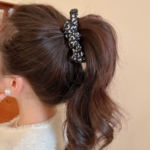 Detailed view of a leopard print fabric hair scrunchie styled on a brunette ponytail