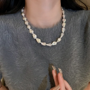 Close-up of irregular white baroque pearl necklace worn over a grey textured sweater