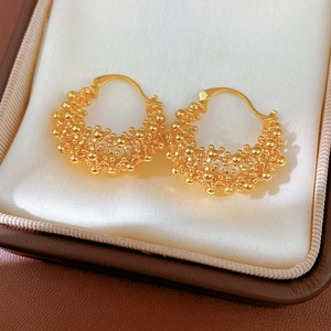 Détail macro de boucles d'oreilles créoles plaquées or 18k avec surface perlée sur satin blanc