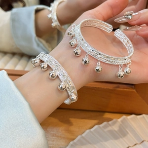 Détail d'un bracelet argenté à cloches et glands porté au poignet sous une lumière chaude