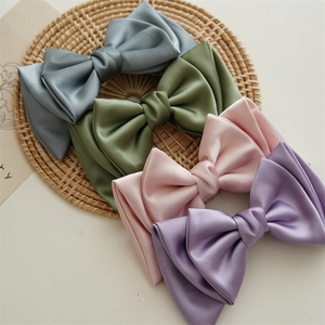 Close-up of four large satin bow hair clips in blue, green, pink and purple on a tray