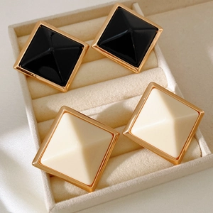Macro shot of geometric square resin stud earrings in black and cream within a jewelry box