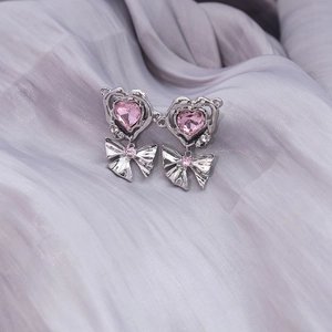 Detail of pink heart-shaped crystal earrings with silver bow design on lilac fabric
