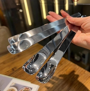 Close-up of four polished stainless steel dessert spoons held by hand in a modern style