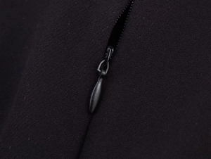 Detailopname van de zwarte jurk met matte ritssluiting en fijn geweven textuur van stof