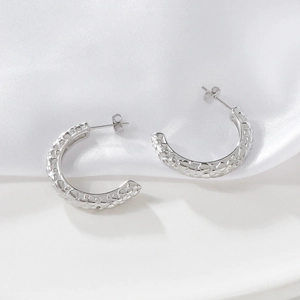 Paire de boucles d'oreilles argentées en C avec relief texturé sur fond de soie blanche