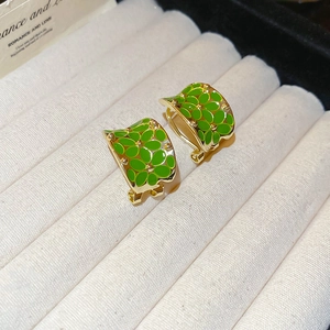 Detail view of green enamel flower earrings with gold metal base in a jewelry box
